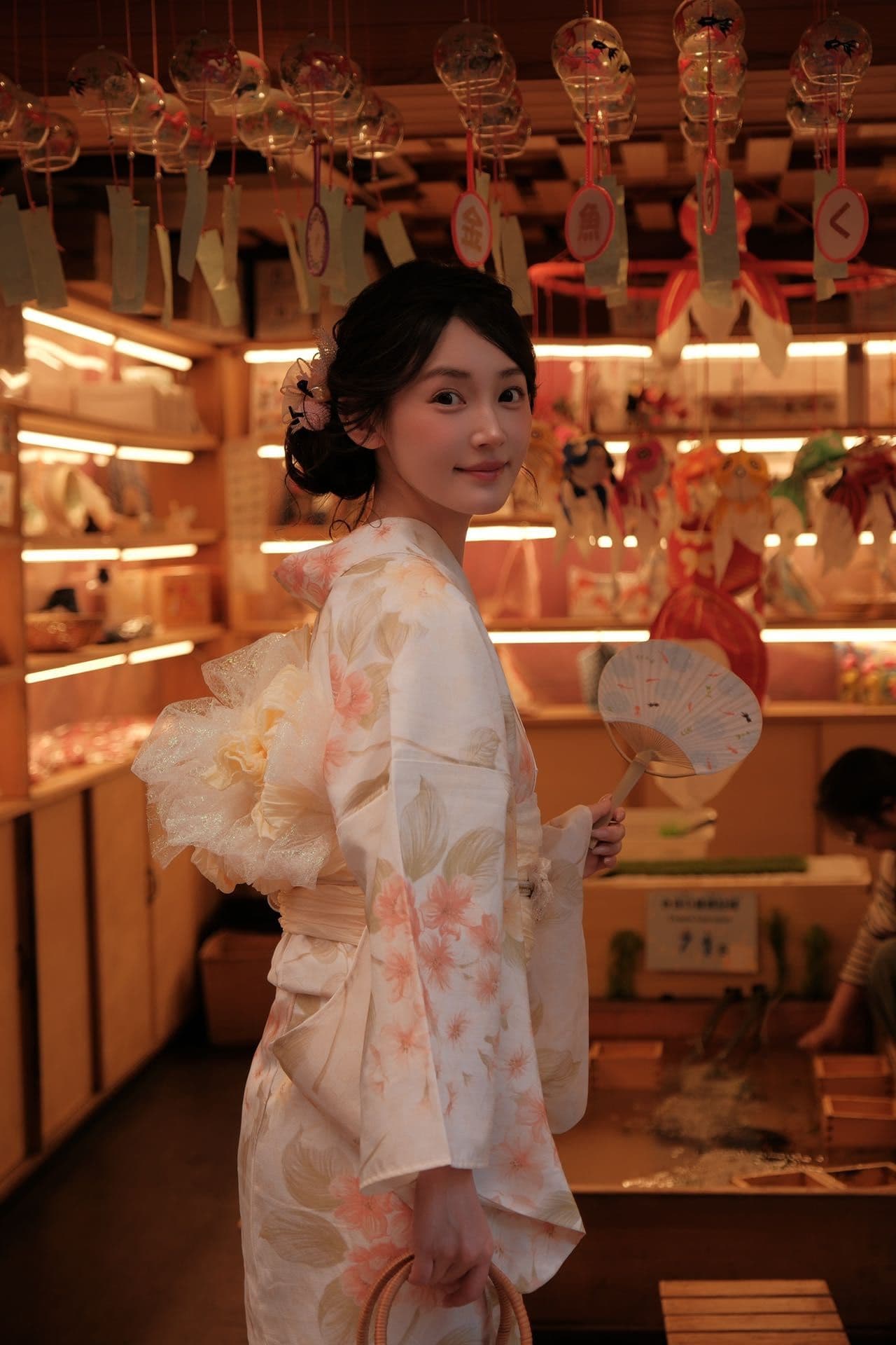 浴衣姿の女性が風鈴の飾られた店内で振り返る、夏のお出かけ風景